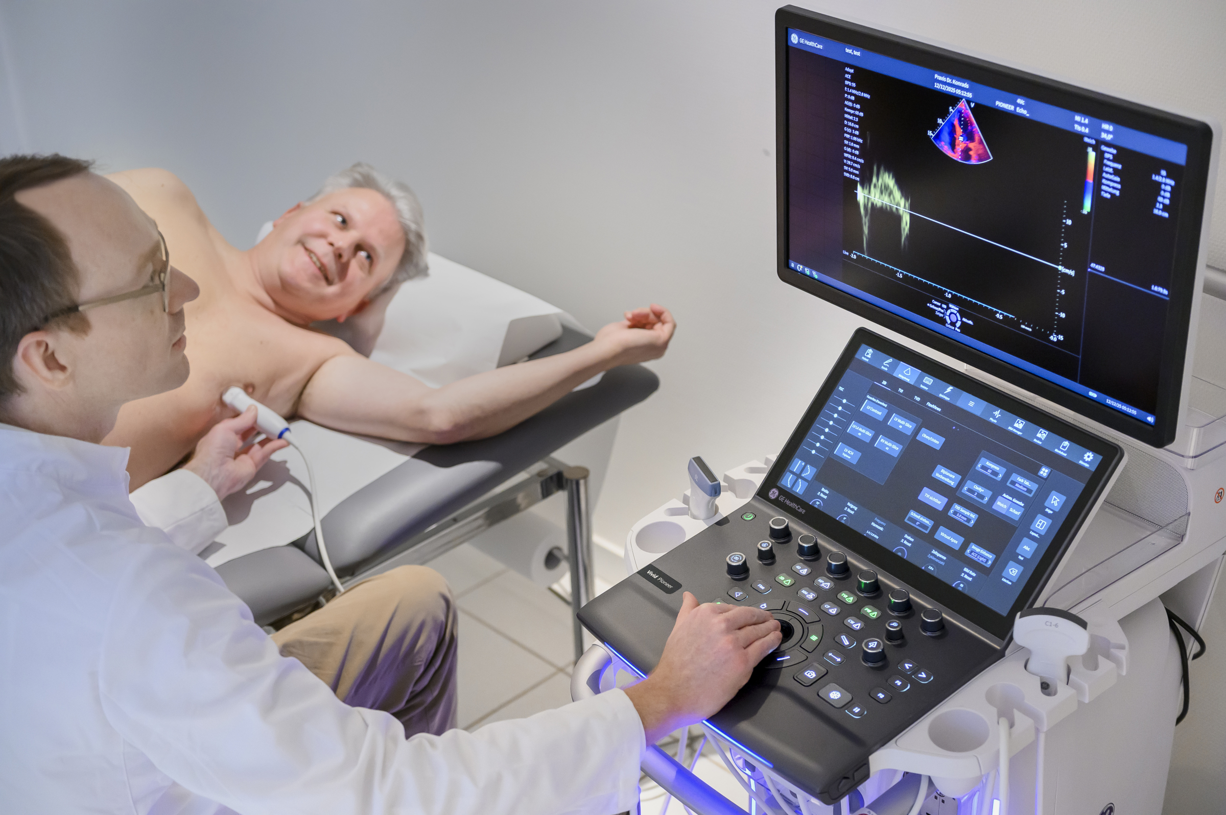 Ein Arzt untersucht das Herz eines männlichen Patienten mit Ultraschall. Beide schauen auf den Monitor.