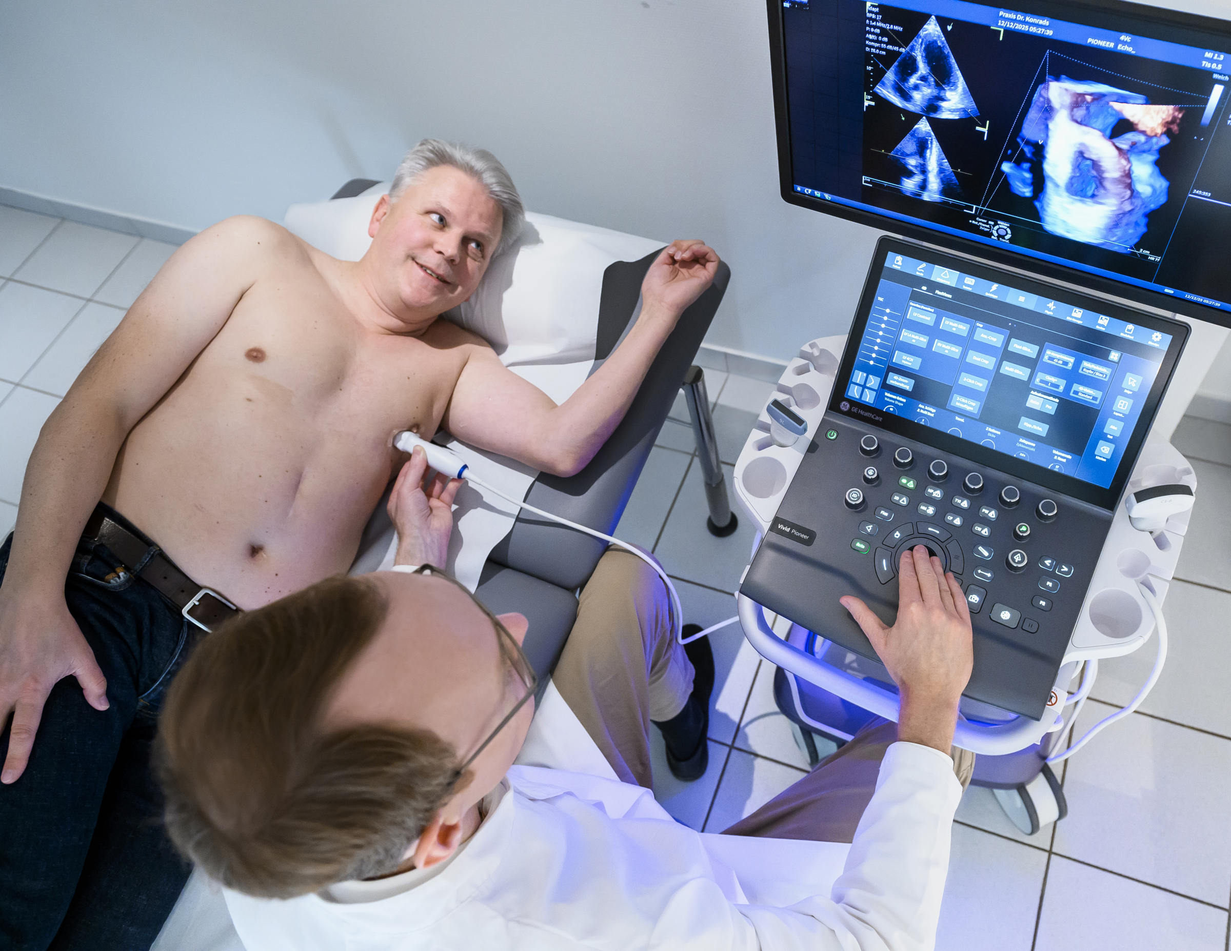 Ein Arzt untersucht das Herz eines männlichen Patienten mit Ultraschall. Beide schauen auf die 3D-Darstellung auf dem Monitor.