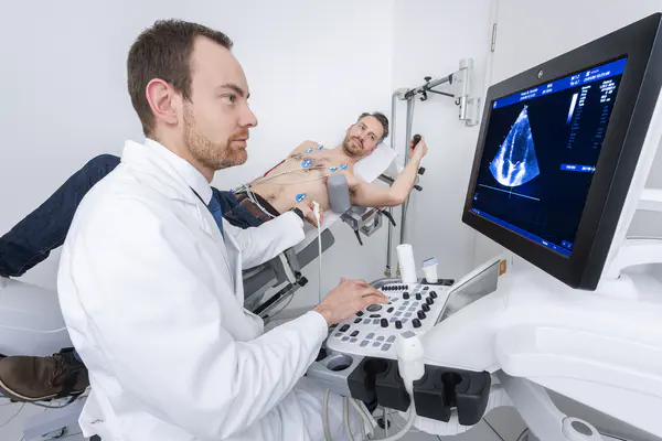 Arzt schaut auf Ultraschallmonitor. Ein Patient auf einem Ergometer.