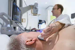 Arzt zeigt auf den Ultraschallmonitor. Patient auf der Liege schaut ebenfalls hin.