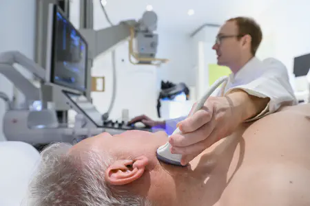 Arzt zeigt auf den Ultraschallmonitor. Patient auf der Liege schaut ebenfalls hin.