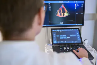 Ein Arzt sitzt am Ultraschallgerät und untersucht einen Mann auf einer Liege.