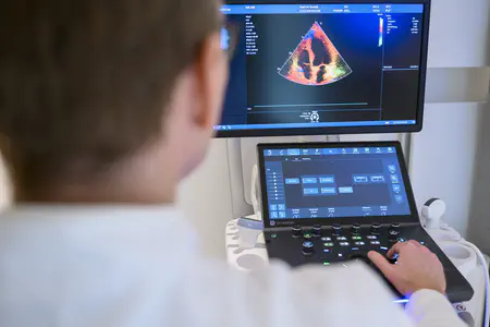 Ein Arzt sitzt am Ultraschallgerät und untersucht einen Mann auf einer Liege.