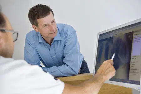 Patient beugt sich vor, um auf den Monitor zu schauen. Der Arzt erklärt etwas.