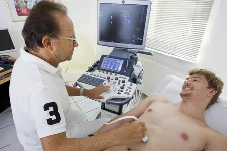 Arzt untersucht Patient auf Liege mit Ultraschall.